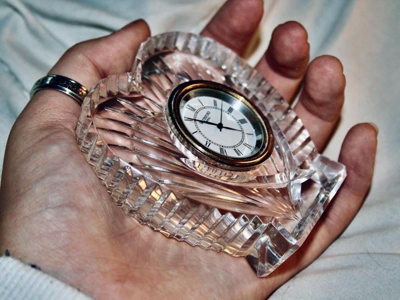 A cold colored hand losing grip with a heart shaped glass clock rested the palm of a hand. 