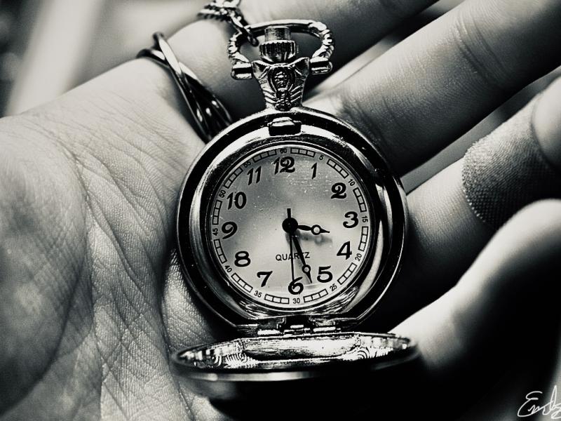 A black and white depiction of a hand holding “time” an open pocket watch 