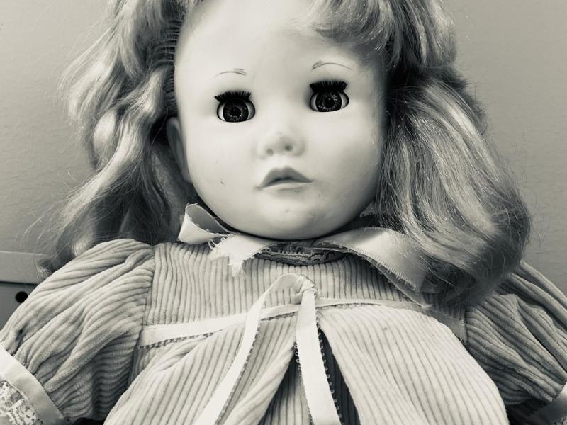 A child's baby-doll staring creepily from the shelf of a second hand store. This image is in black and white.