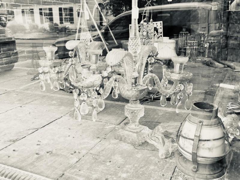 assorted antiques in the shop window messily arranged. This image is in black and white.