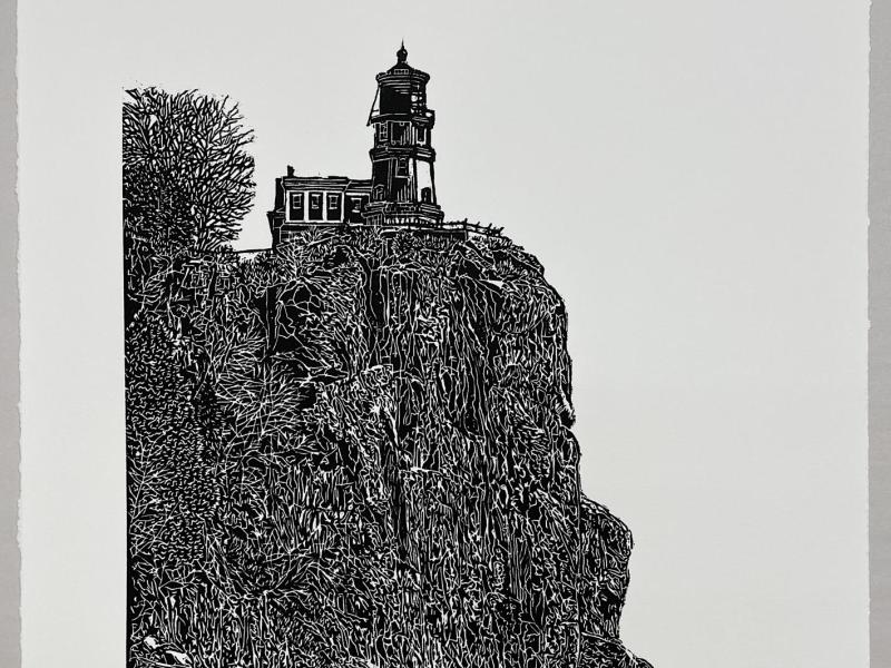 A carved image of Split Rock Lighthouse located on Lake Superior. It is a black and white, carved relief print that is incredibly dense and detailed depicting the light house, rocky ledge, and shoreline.