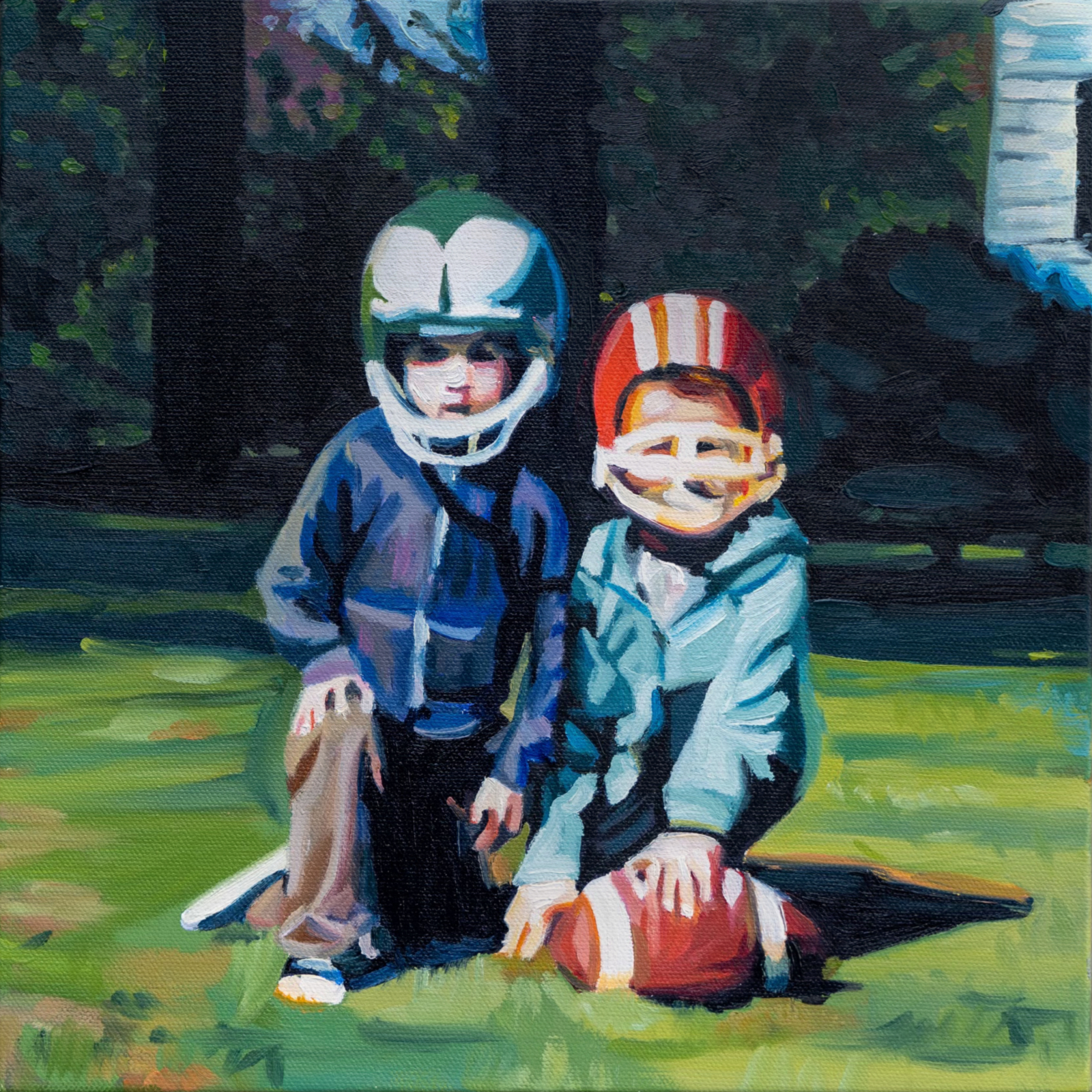 Two brothers kneeling down posting with their football helmets and a football. They look serious, but their helmets are too big. There is greenery in the background. 