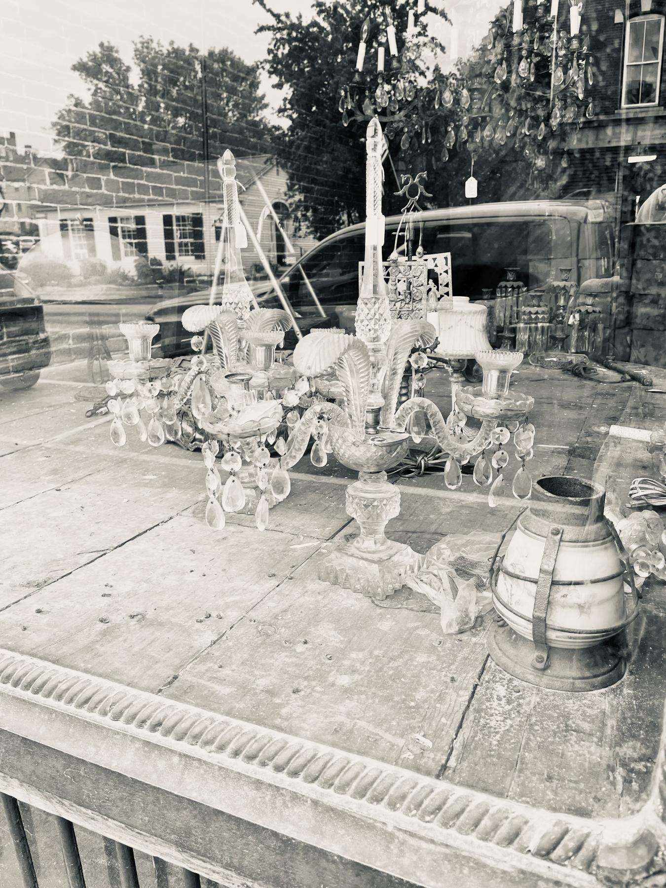 assorted antiques in the shop window messily arranged. This image is in black and white.