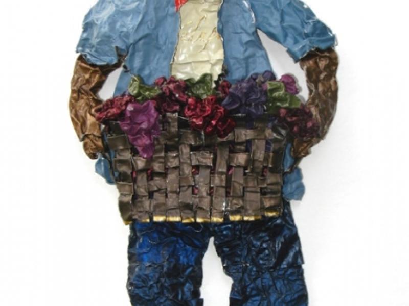 A sculpture on paper made from wine capsules of a field worker carrying a basket of grapes 
