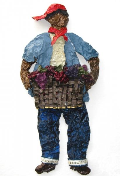 A sculpture on paper made from wine capsules of a field worker carrying a basket of grapes 