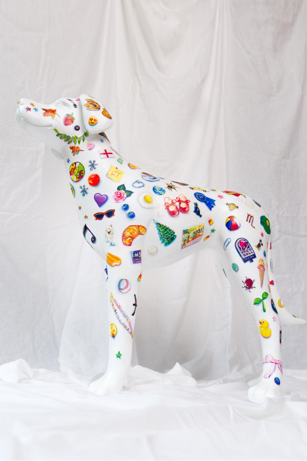 A white dog sculpture painted with dozens of tiny little objects, such as hearts, fruit, plants, logos, toys, etc. 